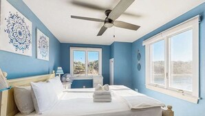Een slaapkamer met een bed, een plafondventilator, een raam met uitzicht en kunst aan de muur.