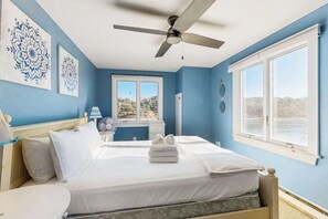 Un dormitorio con cama, ventilador de techo, ventana con vistas y obras de arte en la pared.