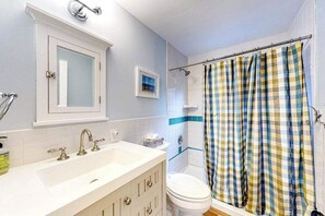 Een badkamer met een wit wastafelmeubel, een spiegel, een toilet en een douchegordijn.