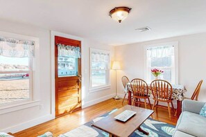 A living room with a wooden door, a dining table with chairs, a sofa, and a lamp. - Inviting cottage with golf nearby, central AC, & full kitchen (Cataumet)