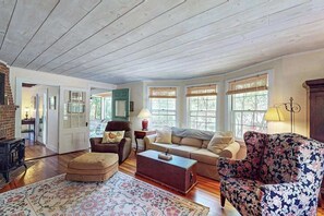 A spacious living room with wooden floors, a fireplace, a sofa, a coffee table, and a patterned rug. - Coastal home with screened porch, W/D, & amazing location (Centerville)
