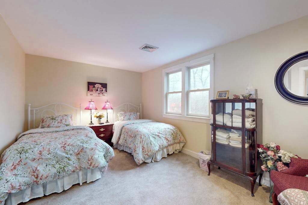 A bedroom with two beds, a dresser, a mirror, and a window.