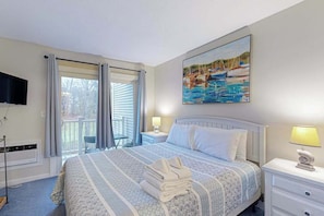 A hotel room with a bed, a painting, a TV, and a balcony.
