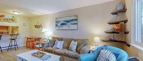 A living room with a sofa, armchair, coffee table, and a painting on the wall.