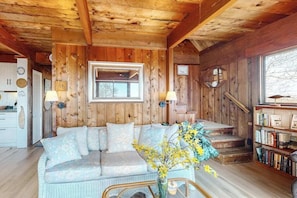 A cozy cabin interior with a sofa, a staircase, and a bookshelf. - Water-view home with large deck, balcony, enclosed sunroom & peaceful location (Aquinnah)