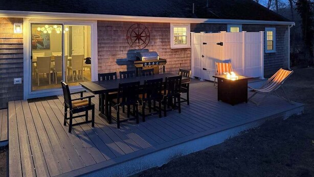 A deck with a grill, dining table, chairs, and a fire pit. - Beautifully renovated home near Scargo Lake with deck, W/D, AC, games, & yard (Dennis)