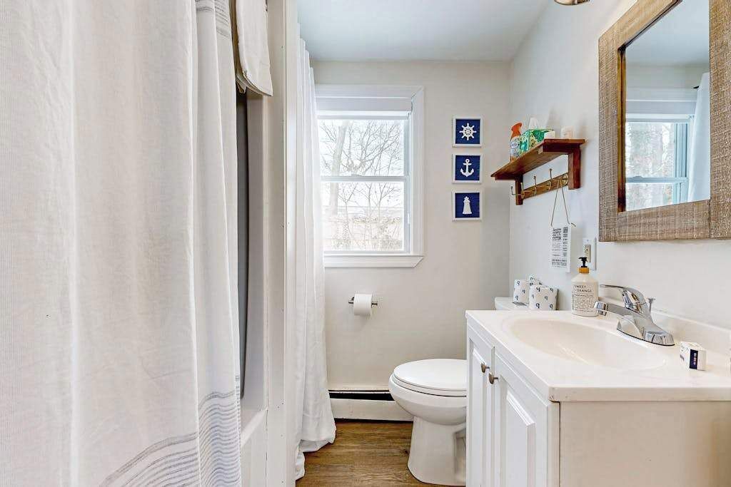 Un baño con inodoro, lavamanos y cortina de ducha. Decoración náutica en la pared.