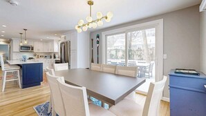 A modern kitchen with white cabinets, a central island, and a dining area with a large table and chairs. - Beautifully renovated home near Scargo Lake with deck, W/D, AC, games, & yard (Dennis)