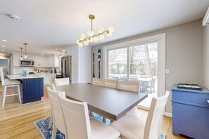 A modern kitchen with white cabinets, a central island, and a dining area with a large table and chairs. - Beautifully renovated home near Scargo Lake with deck, W/D, AC, games, & yard (Dennis)