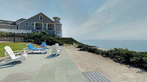 A coastal property with a patio, lounge chairs, and a view of the ocean. - Sleek, modern home with central AC - steps to private beach & near trail (Dennis Port)