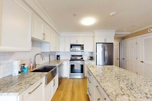 A modern kitchen with white cabinetry, a granite countertop, stainless steel appliances, and a wooden floor.