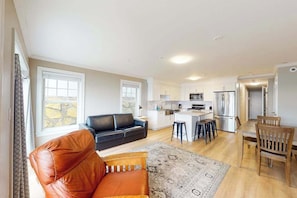 A spacious living area with a sofa, a dining table with chairs, a kitchen with modern appliances, and large windows.