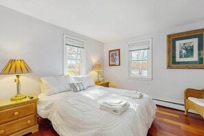 A bedroom with a bed, bedside lamps, a dresser, a chair, and framed pictures on the wall.