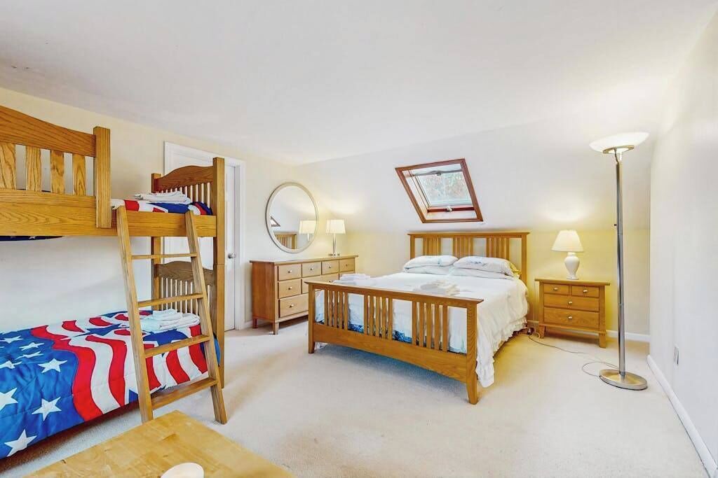 A bedroom with a bunk bed, a single bed, a bedside table, a lamp, a mirror, and a framed picture on the wall.