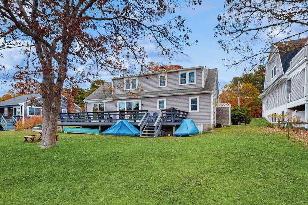 Une maison à deux étages dotée d’une terrasse couverte, d’une pelouse et d’un arbre aux feuilles d’automne.
