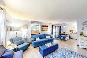 Een woonkamer met een bank, een voetenbankje, en een eethoek met stoelen en een tafel.