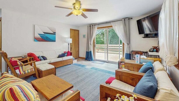 A spacious living room with a ceiling fan, a sofa set, a coffee table, and a TV mounted on the wall.