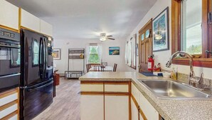 A kitchen with a refrigerator, stove, sink, and a dining area with chairs and a table.