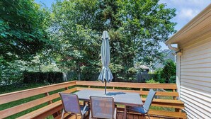 A wooden deck with a table and chairs, surrounded by greenery.