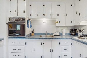 A kitchen with white cabinets, a built-in oven, a sink, and various kitchen appliances. - Welcoming island cottage with patio & enclosed yard - close to town & beaches (Edgartown)