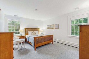 Ein Schlafzimmer mit einem hölzernen Bett, einem Schreibtisch, einem Stuhl und zwei Fenstern.