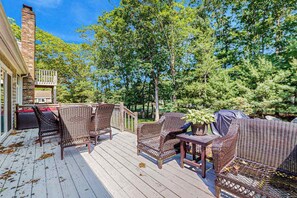 A wooden deck with wicker furniture, a covered table, and a brick chimney. - Peaceful home convenient to bike path, beaches, shopping, dining & entertainment (East Falmouth)