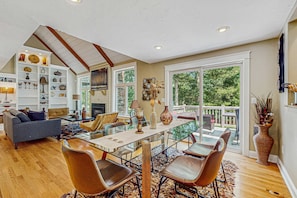 A spacious living area with a glass dining table, leather chairs, a sofa, and a fireplace. - Peaceful home convenient to bike path, beaches, shopping, dining & entertainment (East Falmouth)