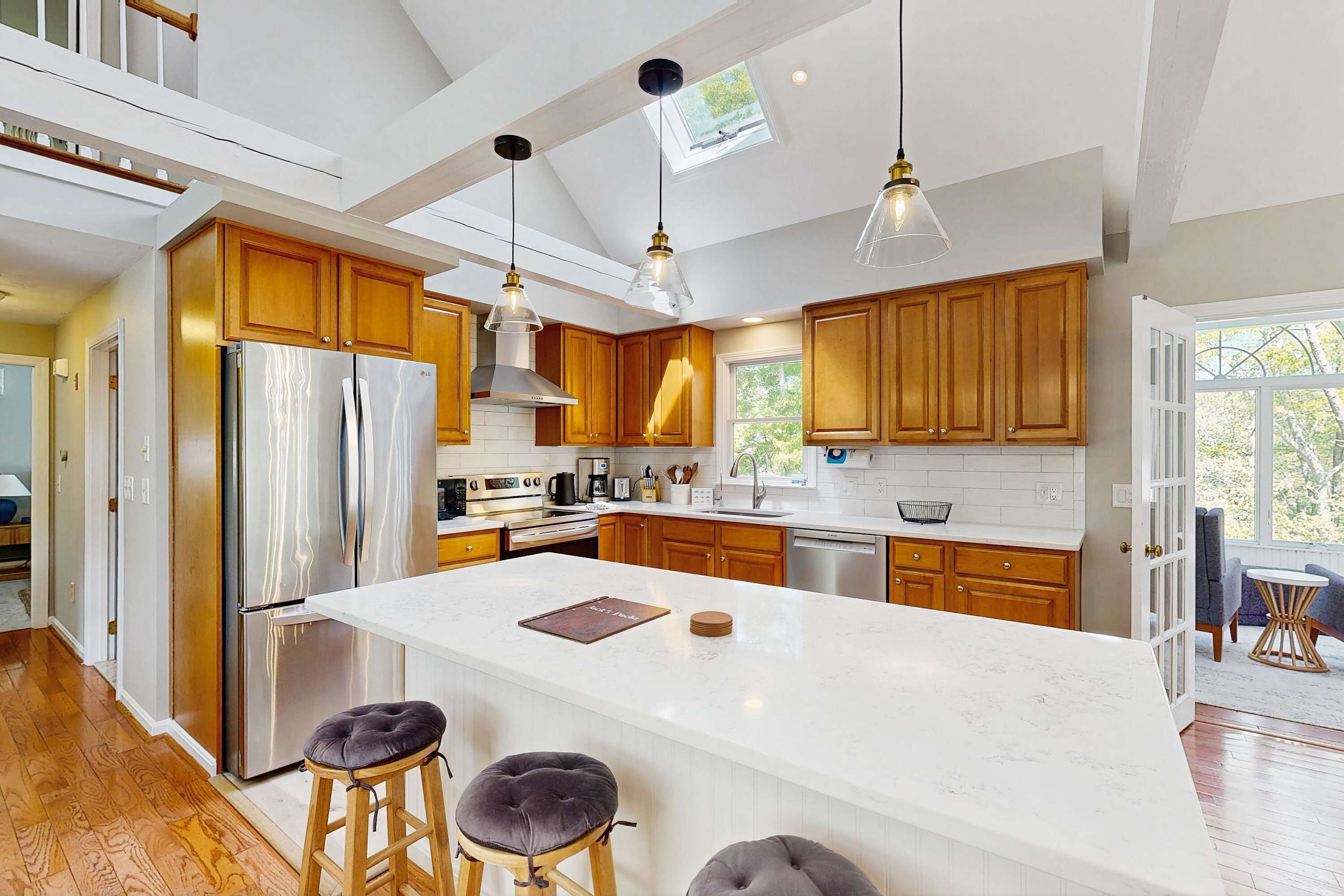 A modern kitchen with a large island, wooden cabinets, stainless steel appliances, and pendant lighting.