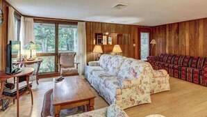 A living room with a sofa, armchair, coffee table, and a television. - Comfy Cabin with Deck, Firepit, & Bike Path Access - Walk to Nauset Light Beach (Eastham)