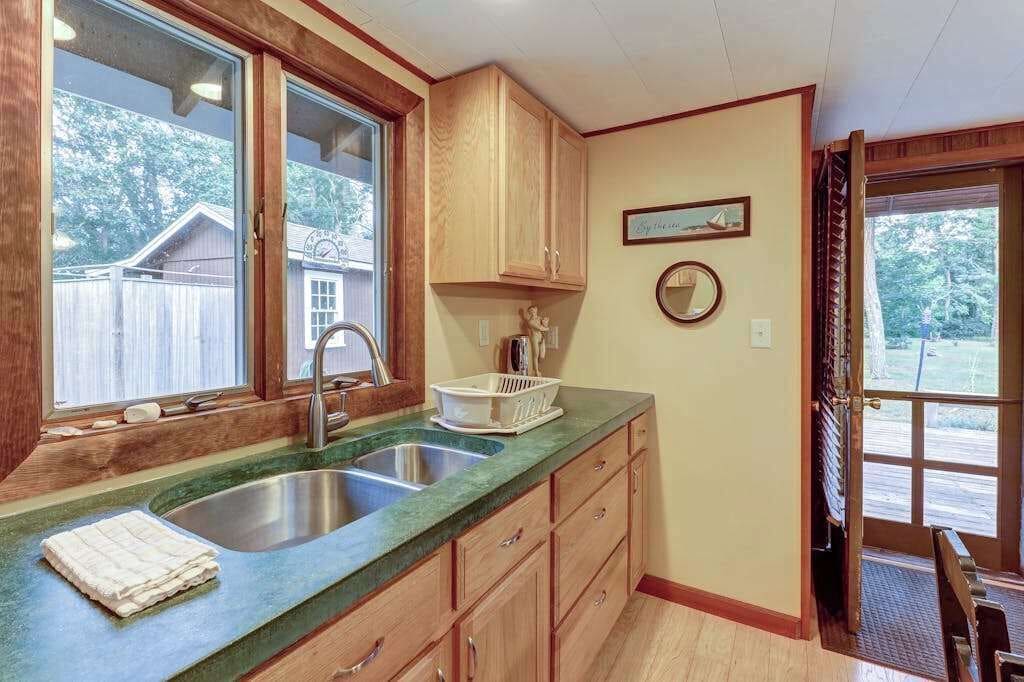 Une cuisine avec deux éviers, des meubles de rangement en bois, une fenêtre et une porte donnant sur l’extérieur.