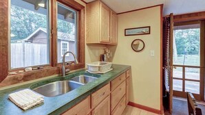 A kitchen with two sinks, wooden cabinets, a window, and a door leading outside. - Comfy Cabin with Deck, Firepit, & Bike Path Access - Walk to Nauset Light Beach (Eastham)