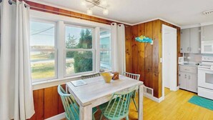 A kitchen with a dining table and chairs, wooden walls, a window with curtains, and a microwave. - Peaceful waterview retreat with sunroom, AC, grill & amazing outdoor space (Eastham)
