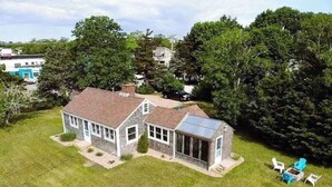 A two-story house with a large backyard, a garage, and a detached garage. - Peaceful waterview retreat with sunroom, AC, grill & amazing outdoor space (Eastham)