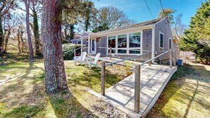 Een gelijkvloers huis met een veranda, een trap en een grote boom op de voorgrond.