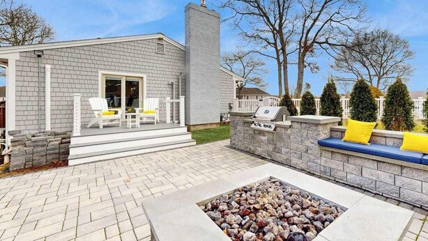 Ein Haus mit Terrasse, Sitzgelegenheiten im Freien, einer Feuerstelle und einem Schornstein.