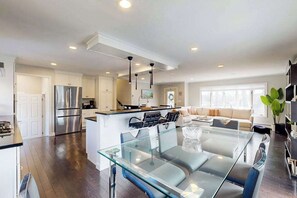 A modern kitchen with a glass dining table, stainless steel appliances, and a central island. - Waterfront home with firepit, grill, open layout, smart TVs, deck, W/D, & AC (East Falmouth)