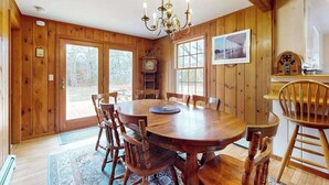 Una sala da pranzo in legno con un lampadario, una sveglia e vista sull'esterno.