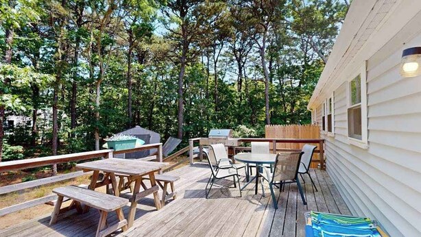 A wooden deck with picnic tables and chairs, surrounded by trees. - Centrally located home near Nauset Light, Coast Guard Beach & Cape Rail Trail (Eastham)
