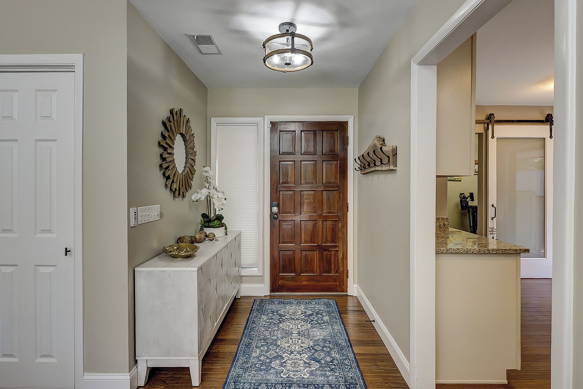 A hallway with a wooden door, a white console table with a bowl, a blue patterned rug, and a ceiling light fixture.