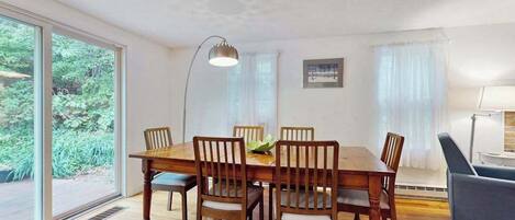 Un comedor con una mesa y sillas de madera, una lámpara de pie y vistas amplias por grandes ventanales.
