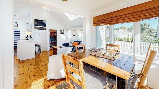 Un'ampia zona giorno con tavolo da pranzo, sedie in legno, divano e cucina sullo sfondo.