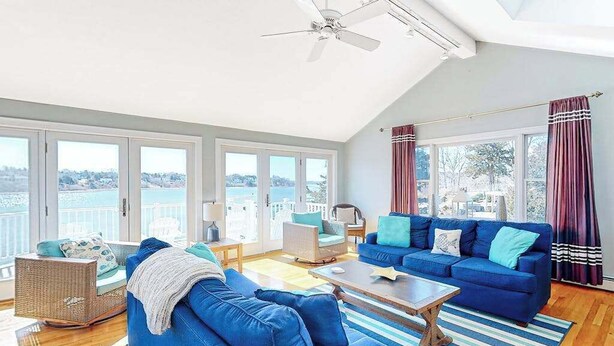Ein großzügiges Wohnzimmer mit einem großen Fenster, einem Deckenventilator und Blick auf das Wasser.