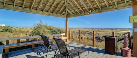 A wooden deck with two chairs and a bench, overlooking a beach and dunes.