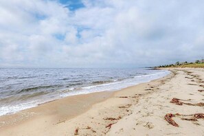 Ein Strand mit Wellen, sandigem Ufer und bewölktem Himmel.