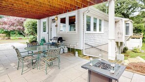 En overdækket terrasse med et glasbord og stole, grill og et vandfald.