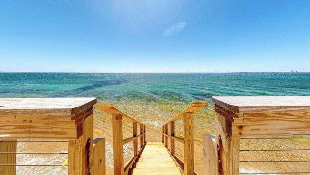 En trätrappa som leder ner till en strand med klart vatten och en klar himmel.