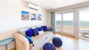 Ett modernt vardagsrum med en soffa, kuddar, ett sidobord och utsikt över havet genom stora skjutdörrar.