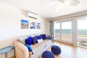 Ein modernes Wohnzimmer mit einer Couch, Kissen, einem Beistelltisch und Meerblick durch große Schiebetüren.