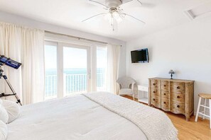 Ein Schlafzimmer mit einem Bett, einem Deckenventilator, einem Fernseher, einem Holzschrank, einem Stuhl und einem Balkon mit Aussicht.