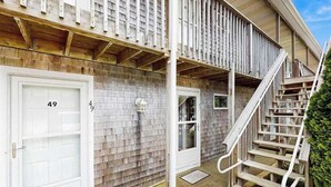 A building with a wooden exterior, a white garage door labeled '49', and a wooden staircase leading to a second-floor balcony. - Cozy, Ground-Floor Getaway w/ Free WiFi, a Kitchen, Shared Pool, & Private Patio (North Truro)